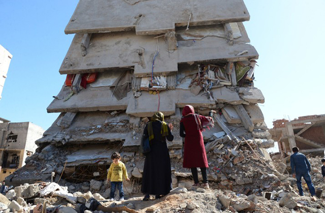 TOPSHOT - People stand among the rubble of damaged buildings following heavy fighting between government troops and Kurdish fighters in the Kurdish town of Cizre in southeastern Turkey, which lies near the border with Syria and Iraq, on March 2, 2016.  Thousands in Turkey's Kurdish-majority town of Cizre started returning to their homes on March 2 after authorities partially lifted a curfew in place since December for a controversial military operation to root out separatist rebels.  / AFP / ILYAS AKENGIN        (Photo credit should read ILYAS AKENGIN/AFP/Getty Images)