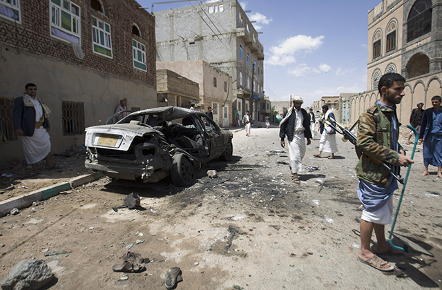 Shiite rebels, known as Houthis, stand near a damaged car after a bomb attack in Sanaa, Yemen, Friday, March 20, 2015. Triple suicide bombers hit a pair of mosques crowded with worshippers in the Yemeni capital, Sanaa, on Friday, causing heavy casualties, according to witnesses. The attackers targeted mosques frequented by Shiite rebels, who have controlled the capital since September. (AP Photo/Hani Mohammed)